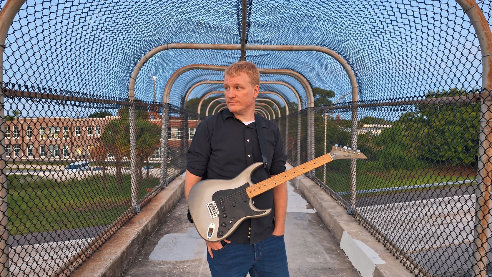 Cedric Harris holding an electric guitar on a St. Petersburg pedestrian overpass