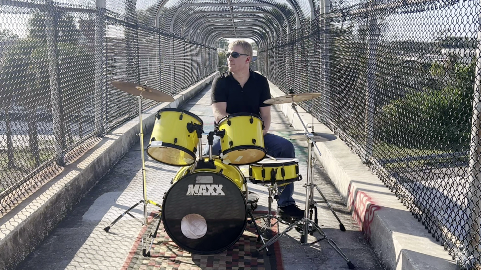 Cedric Harris playing a yellow drum set on a St. Petersburg pedestrian overpass